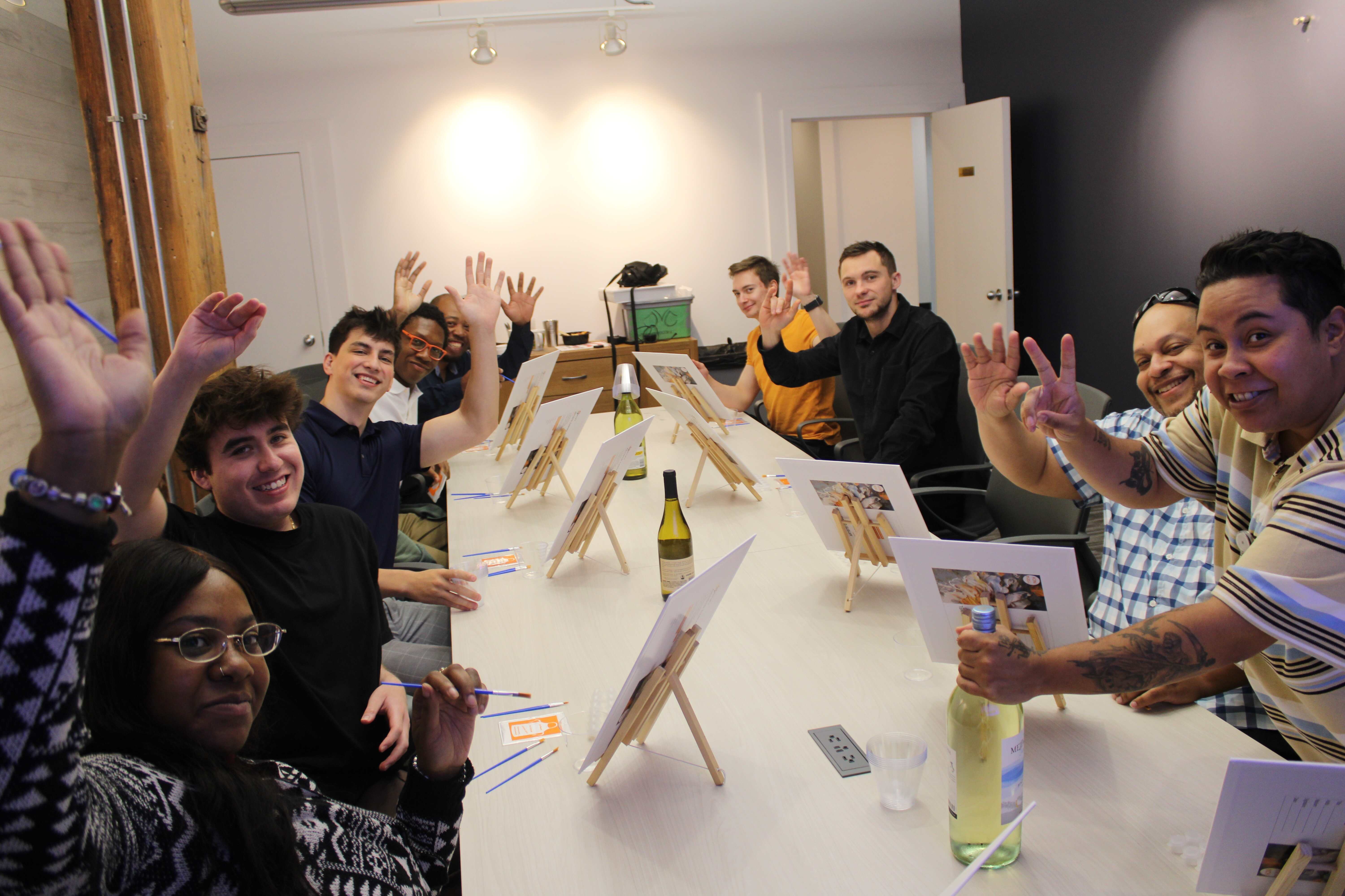 Group of people waving to the camera before starting their paint and sip class at JVC Painting Parties in Chicago, Illinois